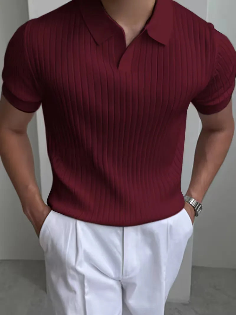 Man draagt bordeauxrode gebreide herenpolo met V-hals en korte mouwen in combinatie met een witte broek.