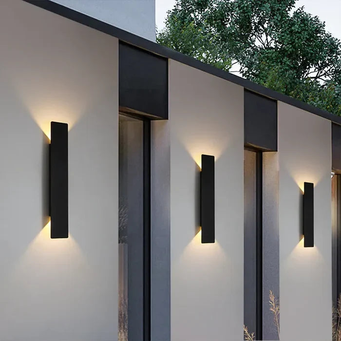 Zwarte StormGlow wandlampen aan een moderne buitenmuur bij schemering.