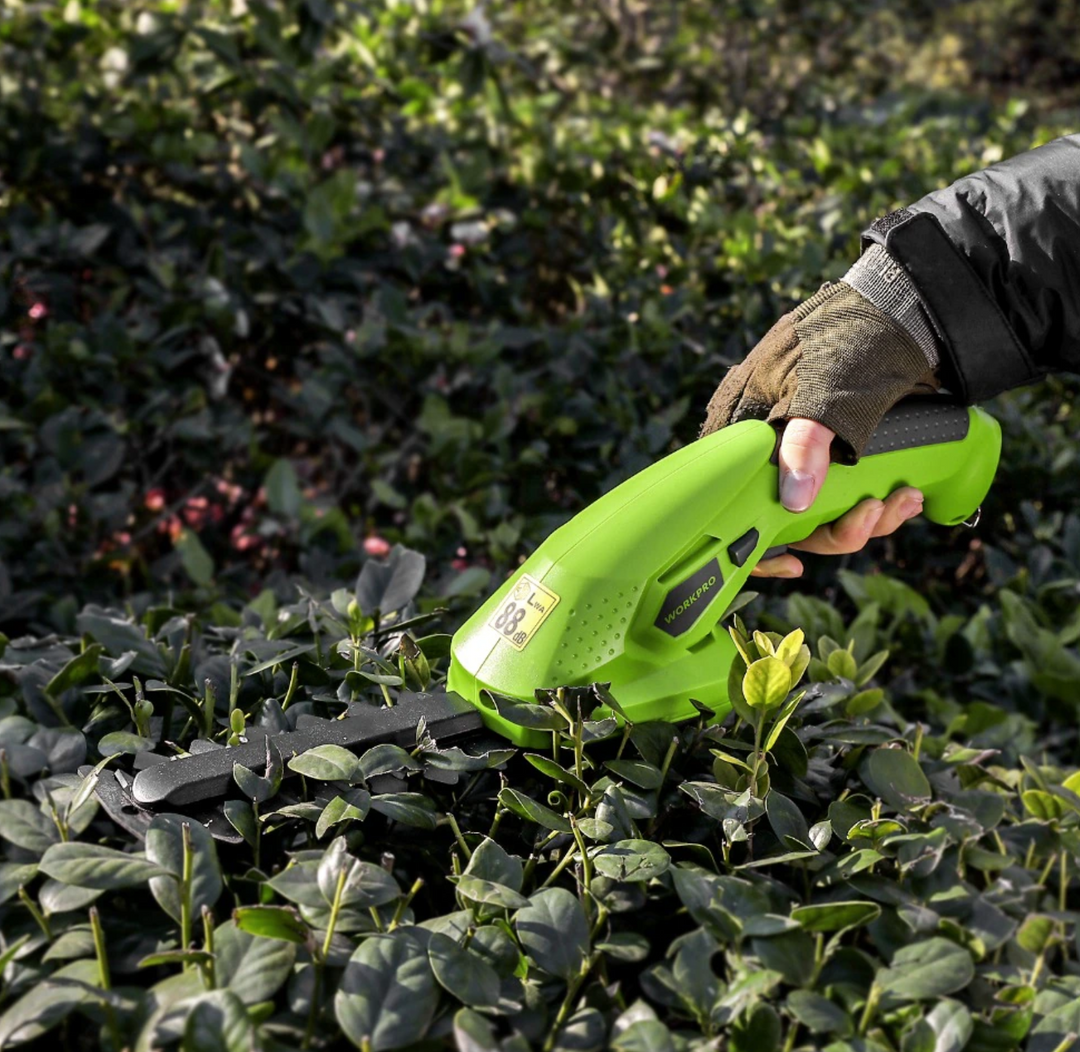 Hand die de groene elektrische heggenschaar vasthoudt tijdens het snoeien van een heg