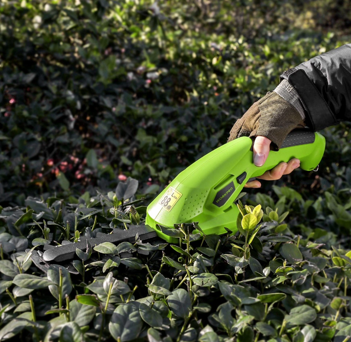 Hand die de groene elektrische heggenschaar vasthoudt tijdens het snoeien van een heg