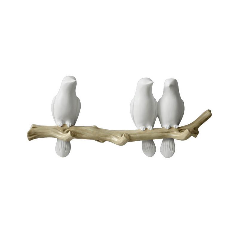 Detail van een witte vogels wandkapstok met drie vogels op een tak, close-up van het design.