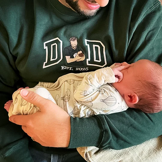 Trots draagt een vader de donkergroene trui met geborduurd familiemoment