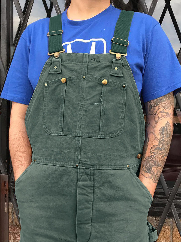Diverse canvas werkoveralls in kameel, groen en zwart. Robuust, functioneel en verstelbaar voor unisex.