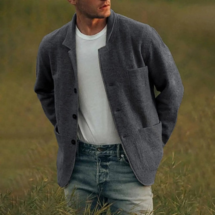 Man toont een donkergrijze casual blazer over een wit T-shirt en spijkerbroek, in een natuurlijke omgeving