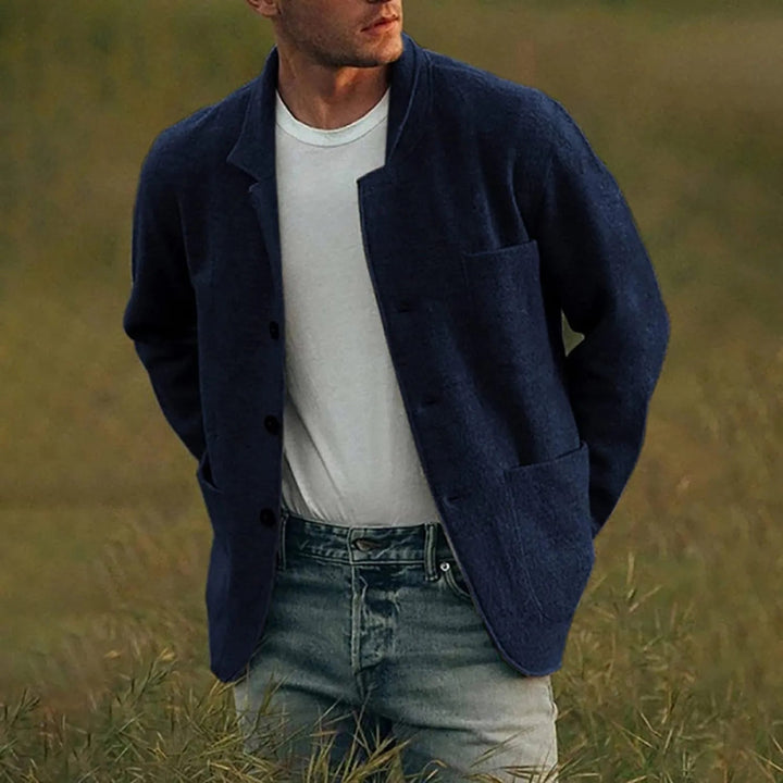 Man draagt een blauwe casual blazer met een wit T-shirt en jeans, poserend in een open veld