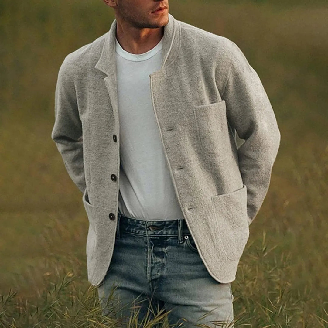 Man in een lichtgrijze casual blazer, gecombineerd met een wit T-shirt en jeans, staand in een groen veld