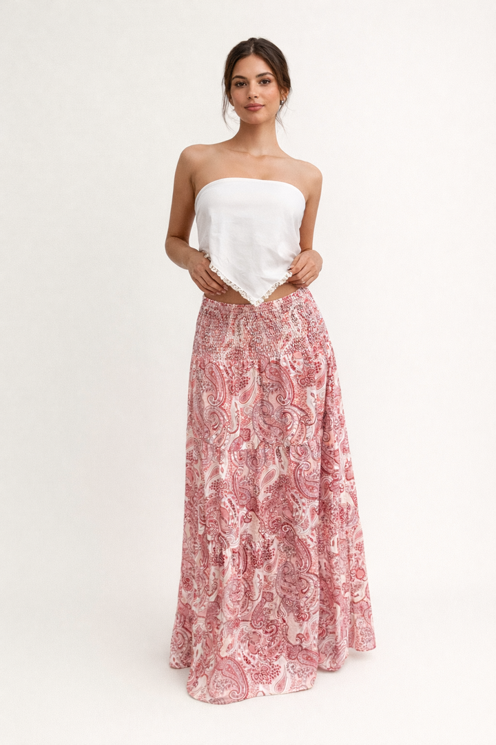 Model poseert met elegante bedrukte maxi rok in roze tinten en een witte strapless top, perfect voor een zomerse dag.