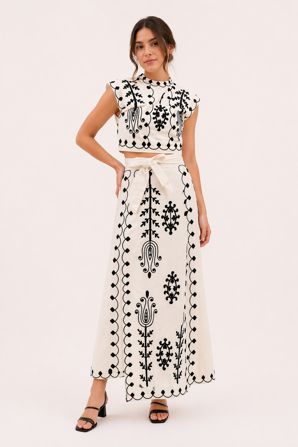 Model draagt een stijlvolle witte geborduurde midirok en top set met zwarte hakken