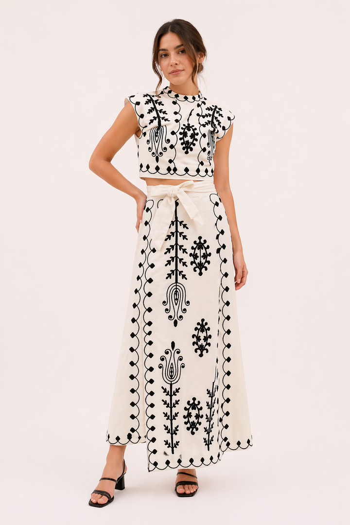 Model draagt een stijlvolle witte geborduurde midirok en top set met zwarte hakken
