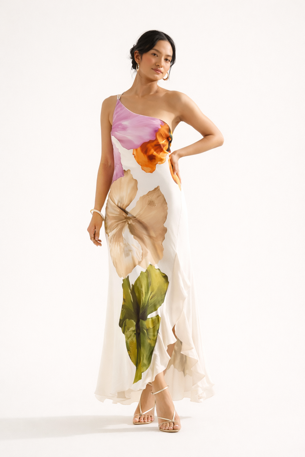 Model draagt een asymmetrische lange witte jurk met kleurrijke bloemenprint en één blote schouder