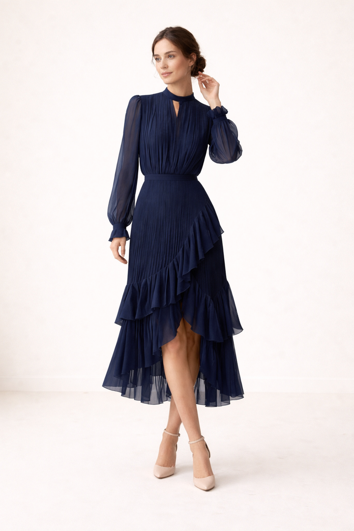 Model draagt marineblauwe plissé midi-jurk met lange mouwen en pumps