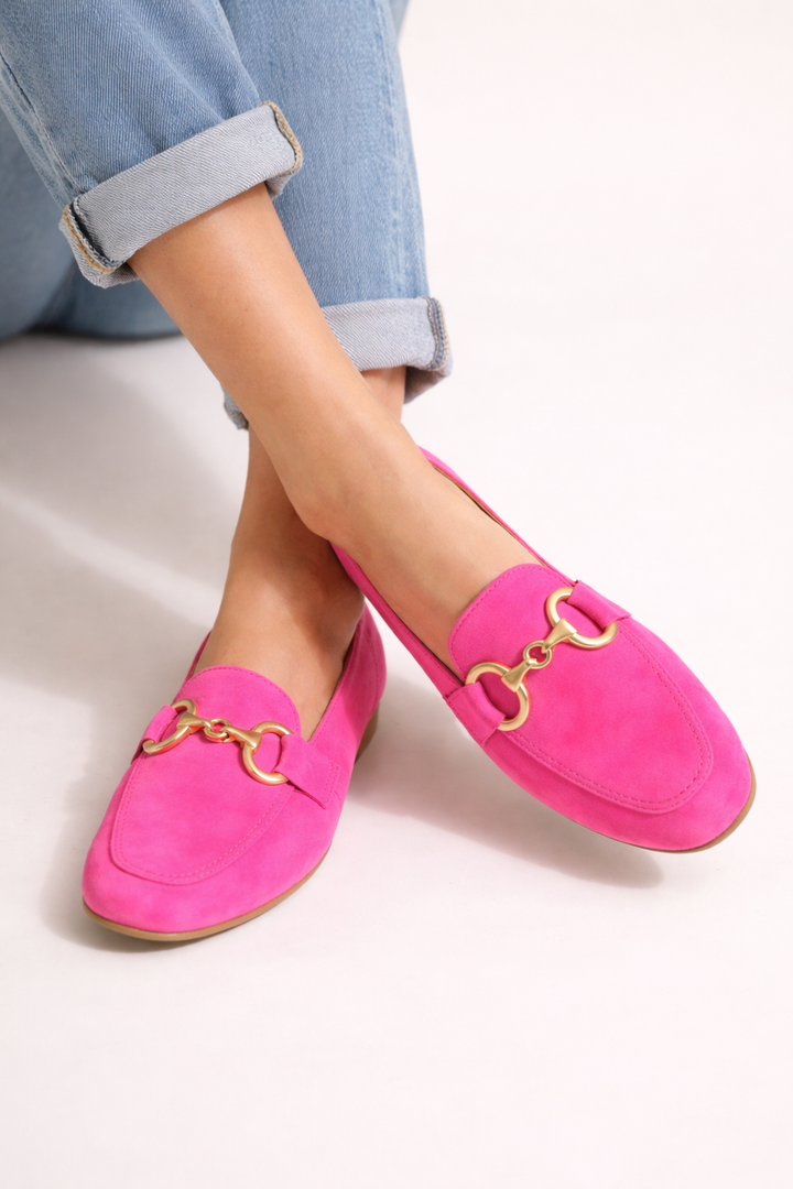 Dames mocassins in helder roze met goudkleurig metallic detail, gedragen met opgerolde jeans.