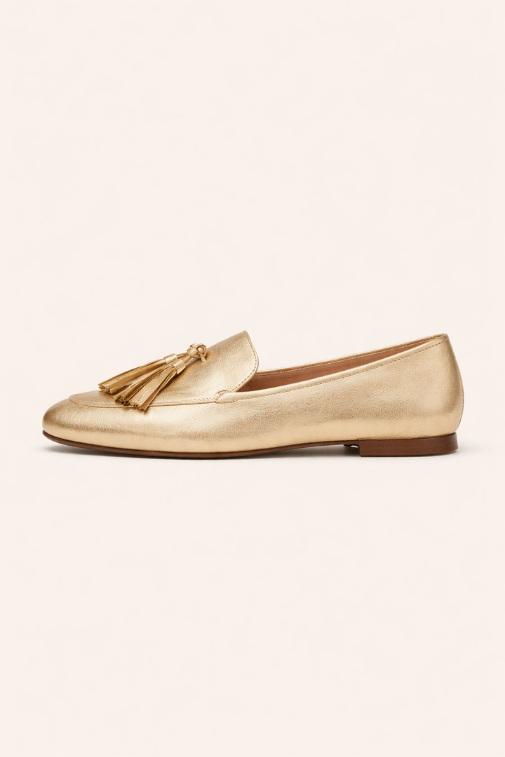 Zijaanzicht van de platte gouden damesschoen met mocassin-stiksels