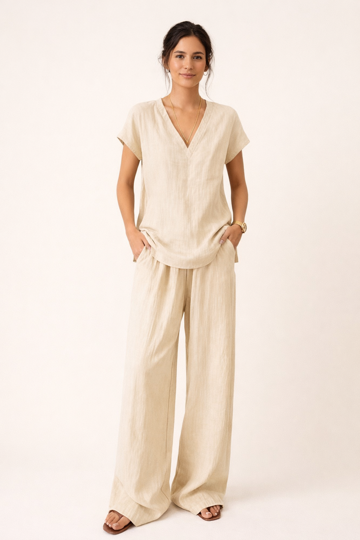 Vrouwelijke model draagt beige tweedelige set met V-hals top en wijde broek, ontspannen en elegant.
