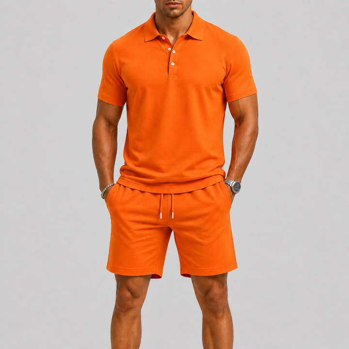 Stijlvolle man met donker haar die een complete oranje heren sportset draagt, bestaande uit een polo en shorts, staand van vo