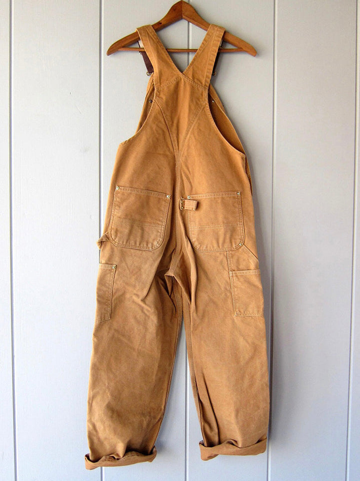 Groene canvas dungarees, stevig en verstelbaar, een functionele werk outfit voor man en vrouw.