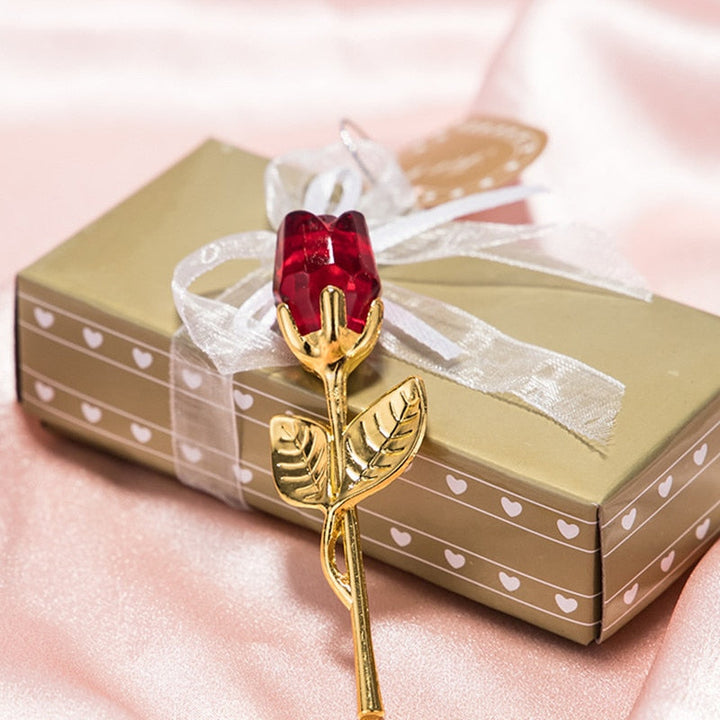 Close-up van een rode glazen roos met gouden details rustend op een elegante geschenkdoos
