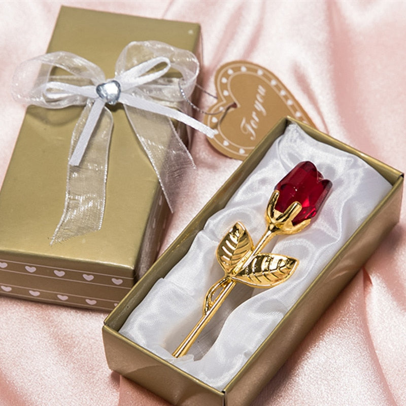 Detailopname van een rode kristallen roos met gouden stengel in een gouden geschenkdoos met strik
