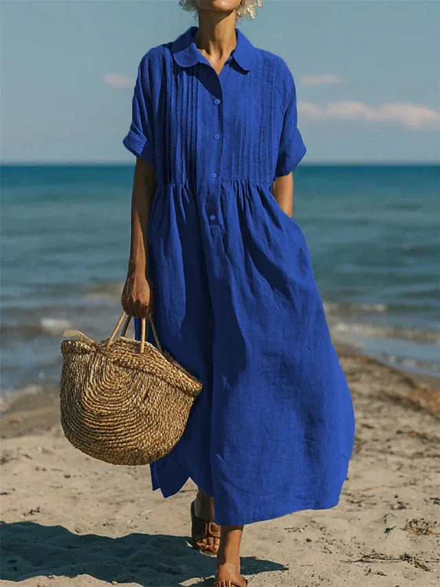 Vrouw loopt op het strand in een elegant blauw hemdblusenkleed, perfect voor zomerse dagen.
