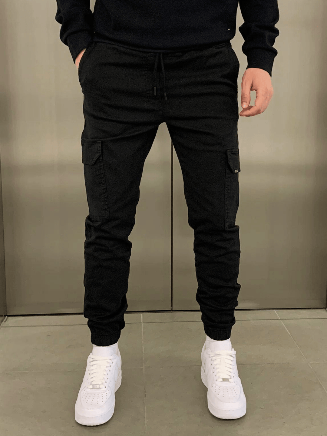 Man draagt zwarte heren lange cargobroek met elastische tailleband en witte sneakers
