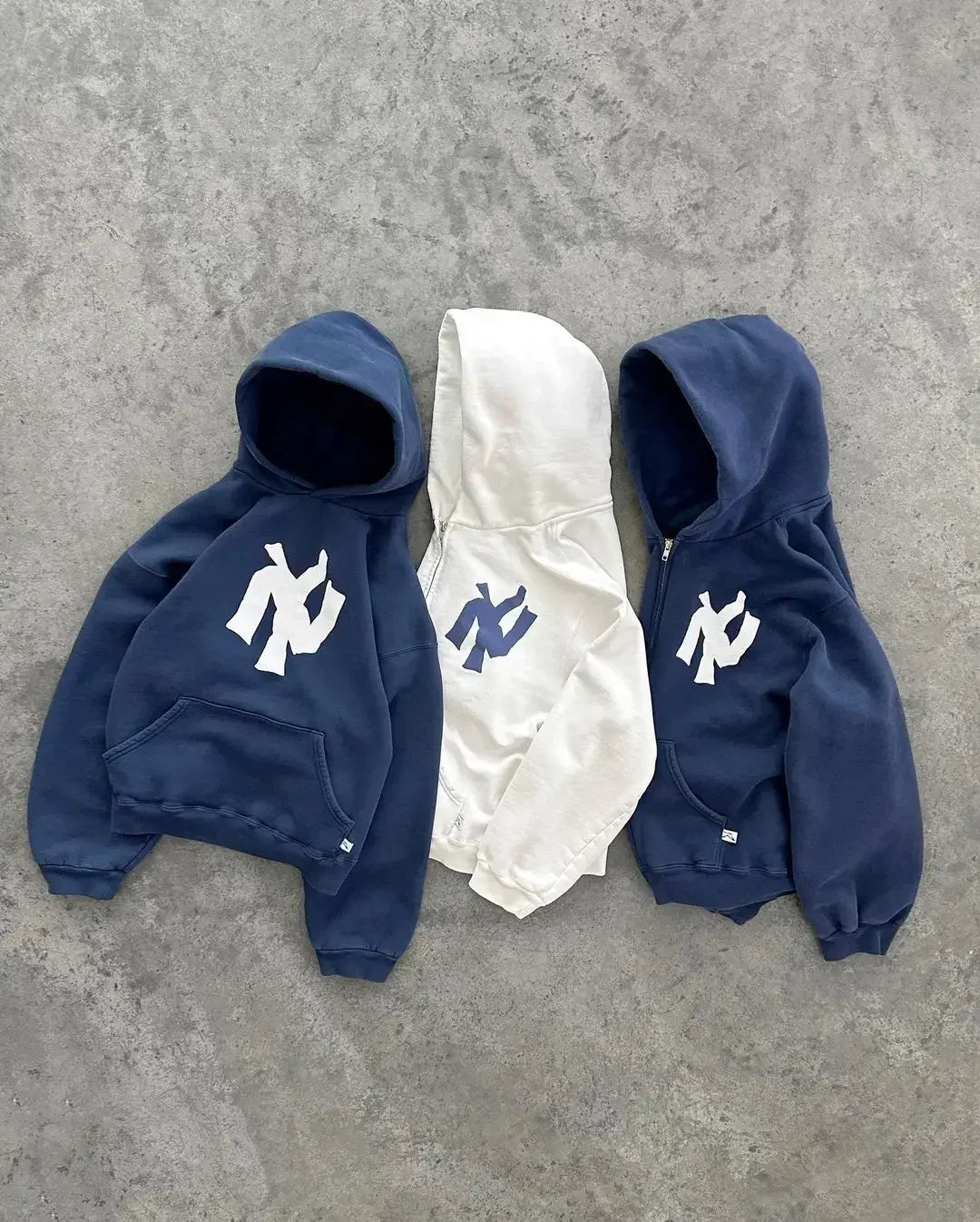 Drie Y2K hoodies en vesten in navy blauw en wit naast elkaar op een betonnen ondergrond