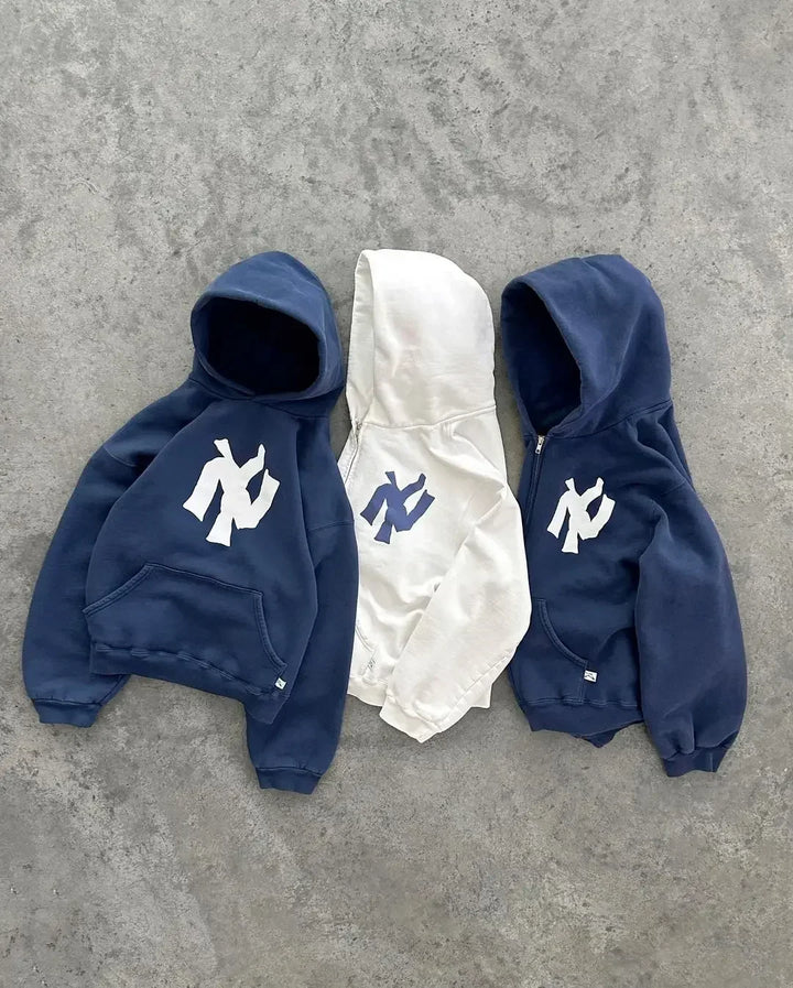 Drie Y2K hoodies en vesten in navy blauw en wit naast elkaar op een betonnen ondergrond