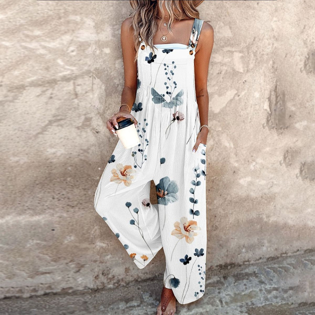 Vrouwelijke model poseert met wit zomer-jumpsuit met bloemenprint tegen een rustieke achtergrond.