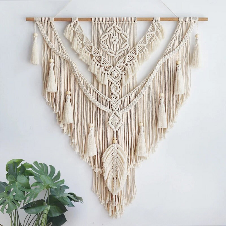 Handgemaakte beige scandinavische macramé wandhanger in boho stijl aan een witte muur