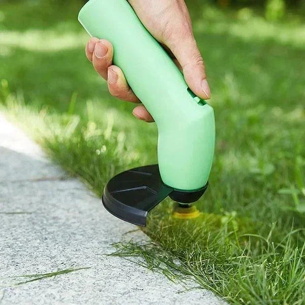 Hand die de groene Taavita draadloze mini grastrimmer vasthoudt boven het gazon