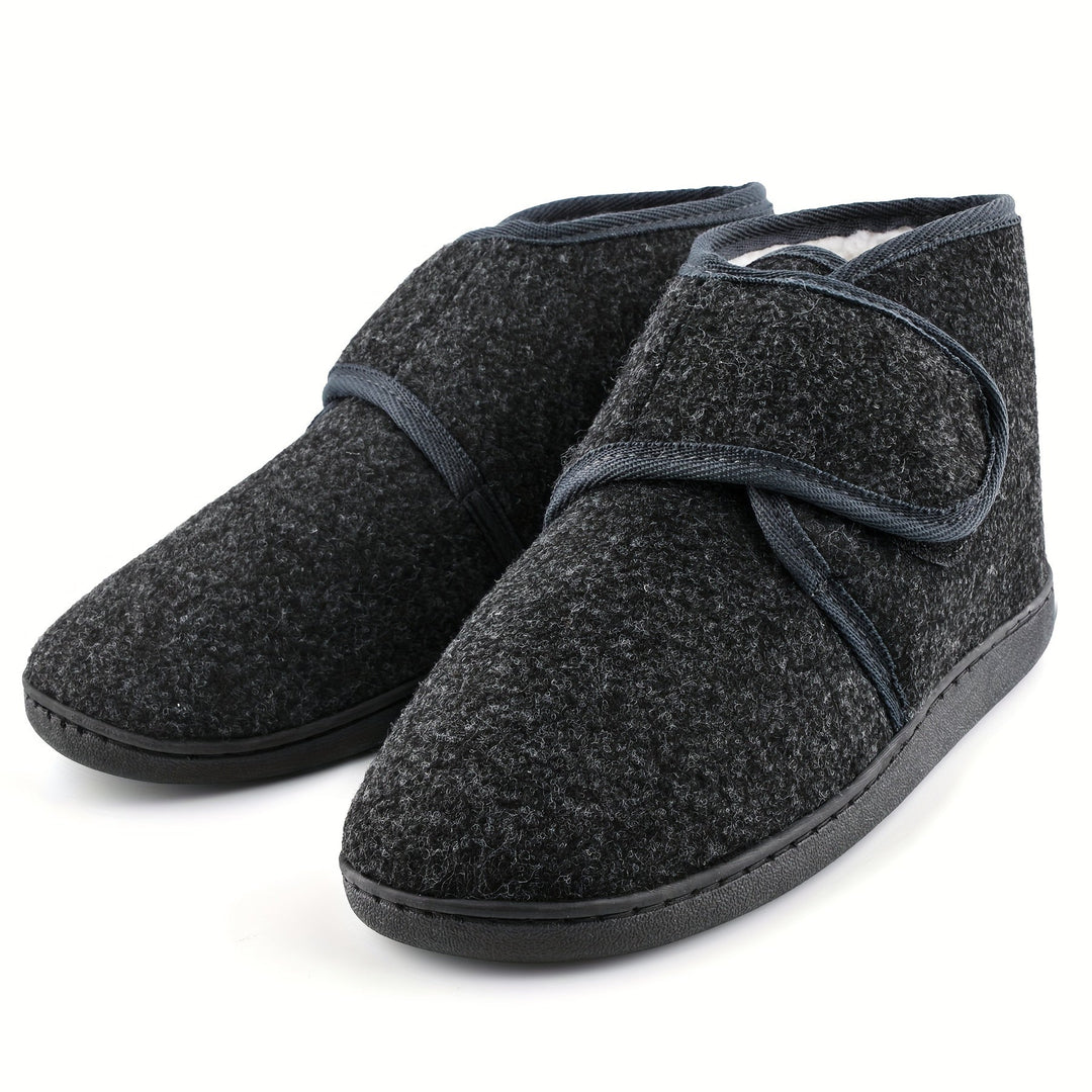 Paar donkergrijze heren pantoffels met klittenbandsluiting en stevige zool, op een witte achtergrond.