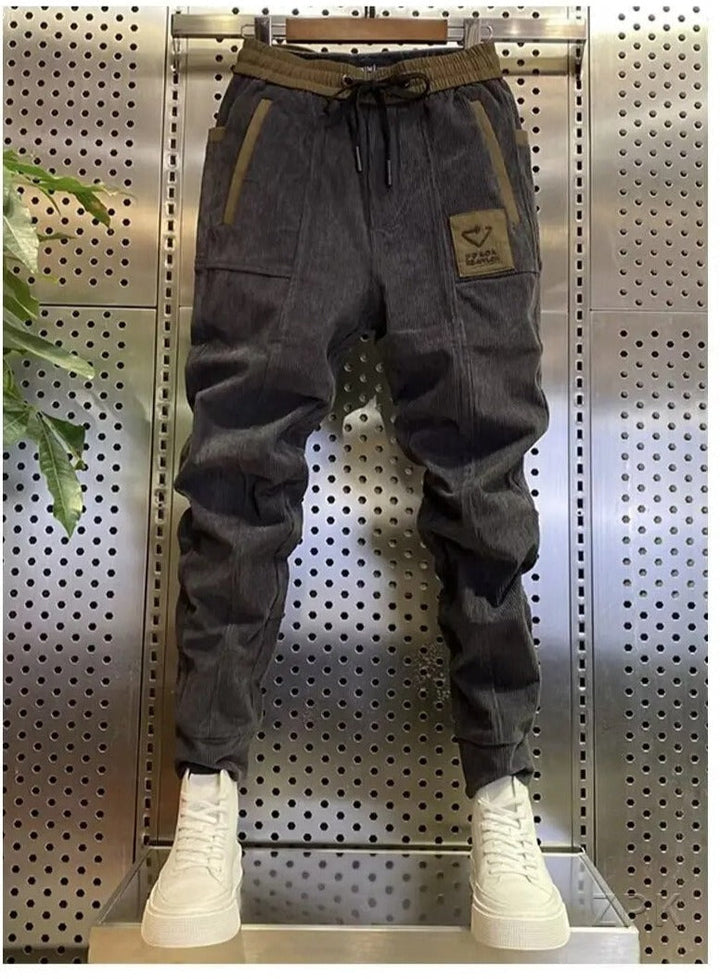 Grijze corduroy cargobroek voor heren, getoond op een mannequin in een moderne setting.