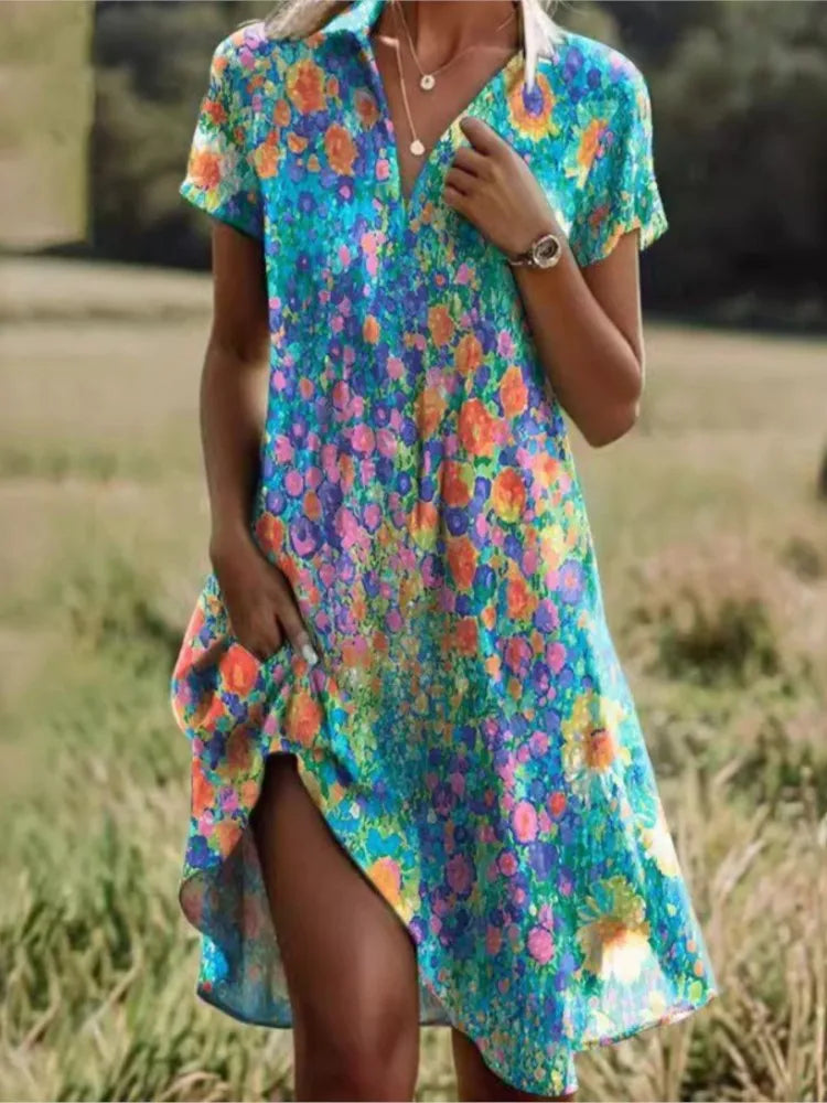 Levendige dames mini overhemdjurk met blauw-roze bloemenprint en V-hals, gedragen in een buitenomgeving.
