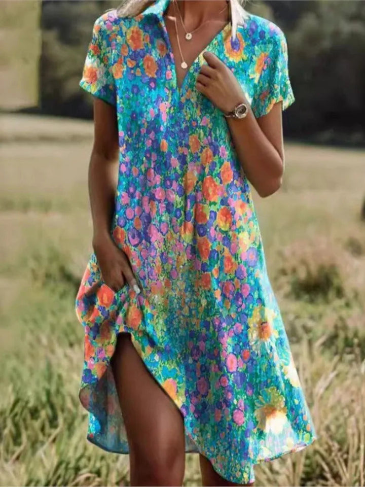 Levendige dames mini overhemdjurk met blauw-roze bloemenprint en V-hals, gedragen in een buitenomgeving.