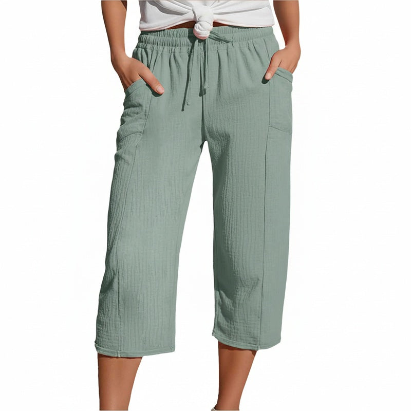 Model in lichtgroene driekwart broek met elastische taille en zijzakken, staand met handen in zakken.
