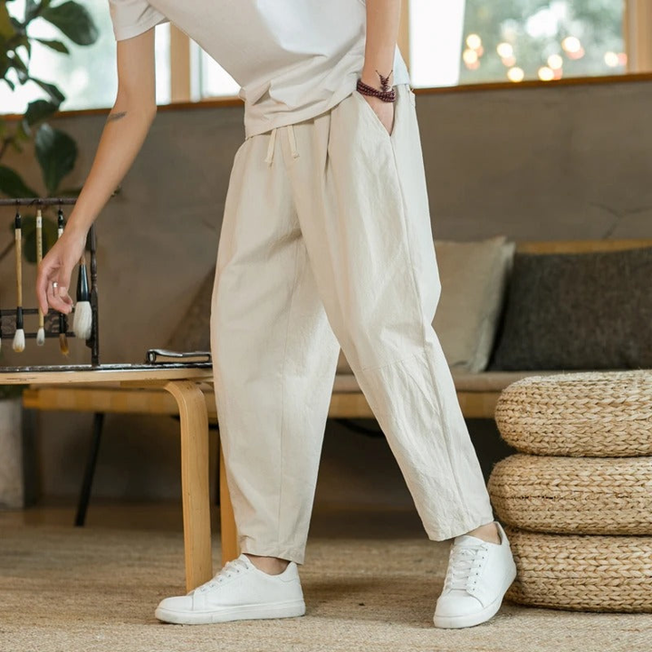 Man draagt een luchtige beige herenbroek met witte schoenen