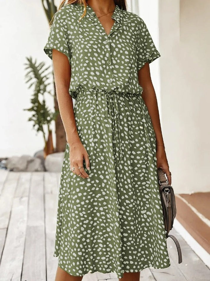 Vrouw draagt een groene midi blousejurk met print in een lichte ruimte