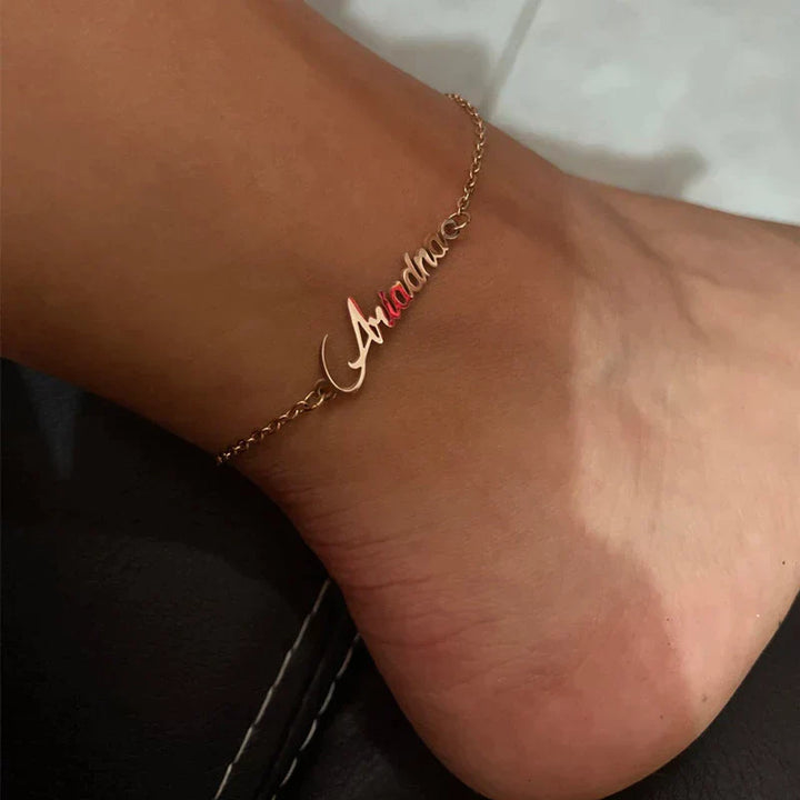 Close-up van een gepersonaliseerd dames enkelbandje met naamletters, handgemaakt en verstelbaar, beschikbaar in goud/zilver.
