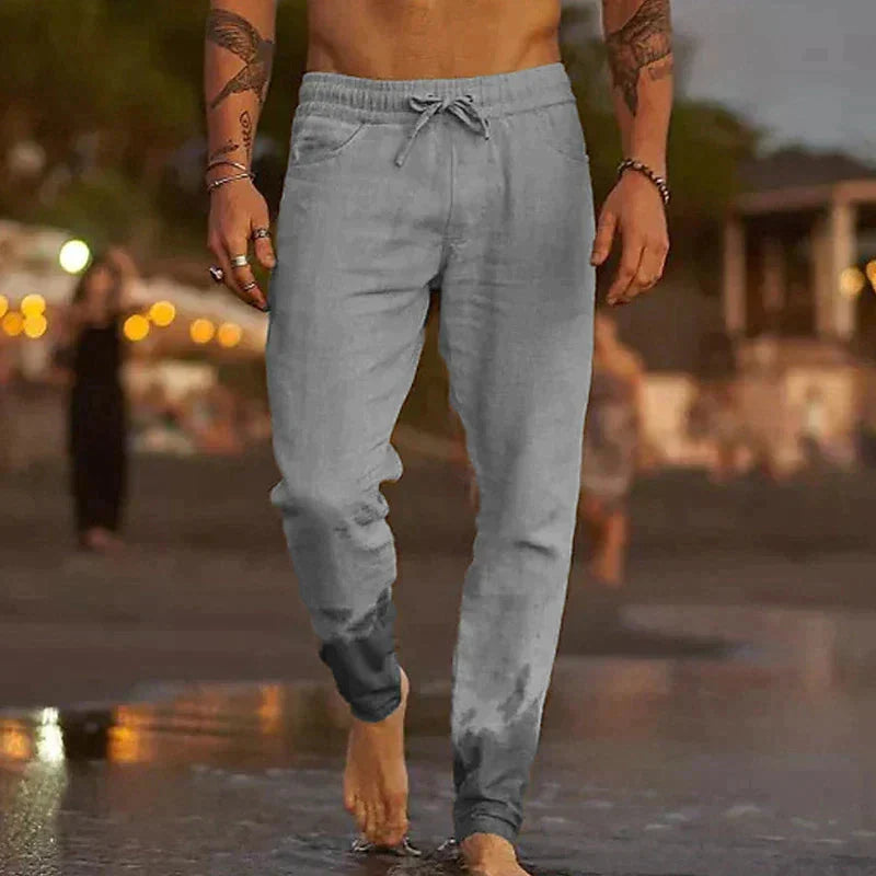 Man loopt in grijze casual broek langs het strand, water raakt zijn enkels [[lstfy-media:3]]