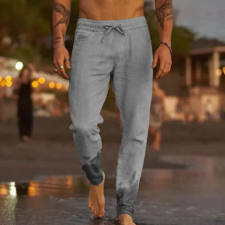 Man loopt in grijze casual broek langs het strand, water raakt zijn enkels [[lstfy-media:3]]