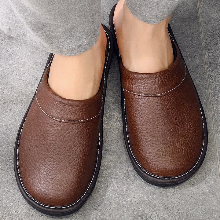 "Heren leren pantoffels met zachte voering, ergonomisch ontwerp en duurzame zool in zwart, getoond op een houten vloer."