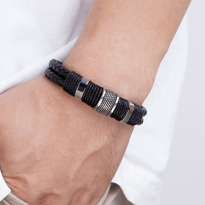 Hand pakt stijlvolle zwarte gevlochten herenarmband met magnetische sluiting, klaar om te dragen.