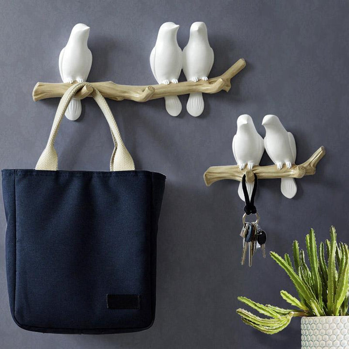 Set van twee witte vogels wandkapstokken met twee en vier haken, versierd met een tas en sleutels.