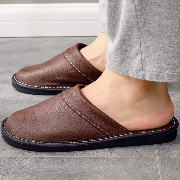 Zijaanzicht van bruine Hugo huisschoenen met witte stiksels op grijze tegelvloer