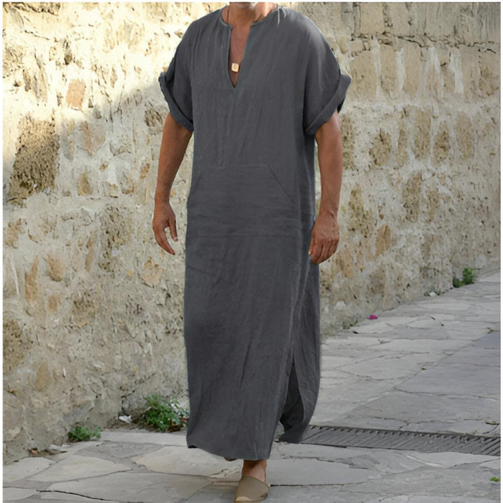 Man in een grijs V-hals lange casual shirt, staand op een geplaveide straat.