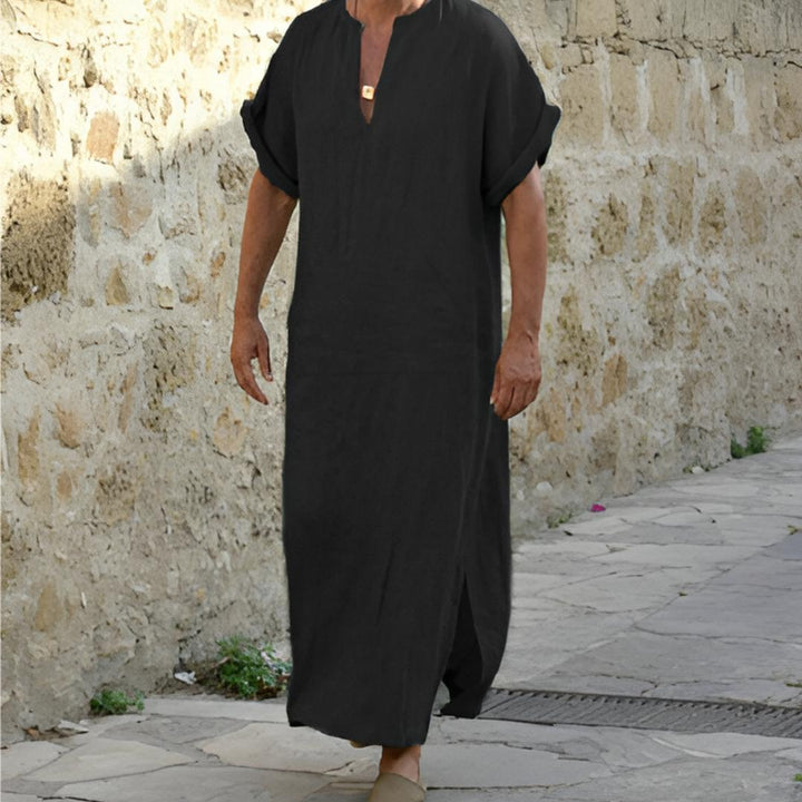Man in een zwart V-hals lange casual shirt, lopend langs een oude stenen muur.