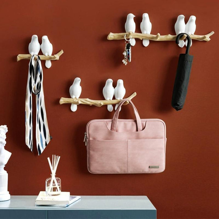 Witte vogels wandkapstok met drie haken aan een tak, waarop een sjaal en een laptoptas hangen.