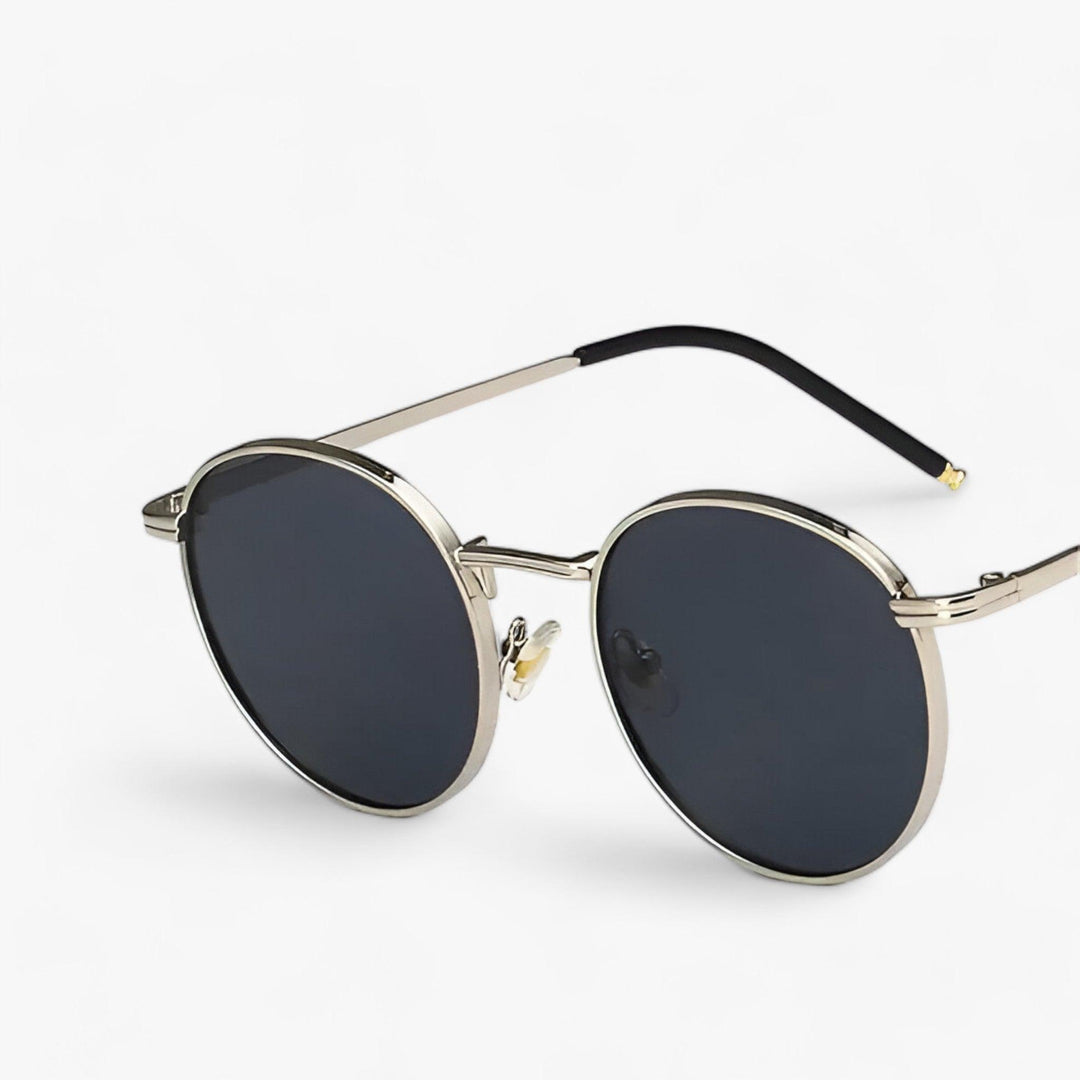 Model draagt trendy uniseks zonnebril met ronde glazen en metalen frame, genietend van de zon met UV-bescherming.