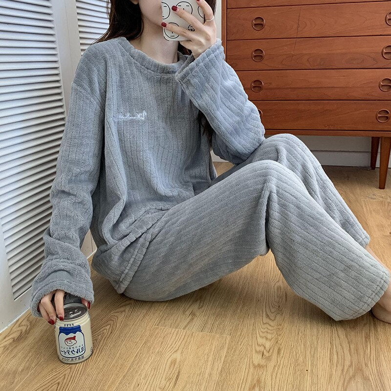 Vrouw draagt warme koraalfleece damespyjama. Comfortabele 2-delige loungewear voor thuis.